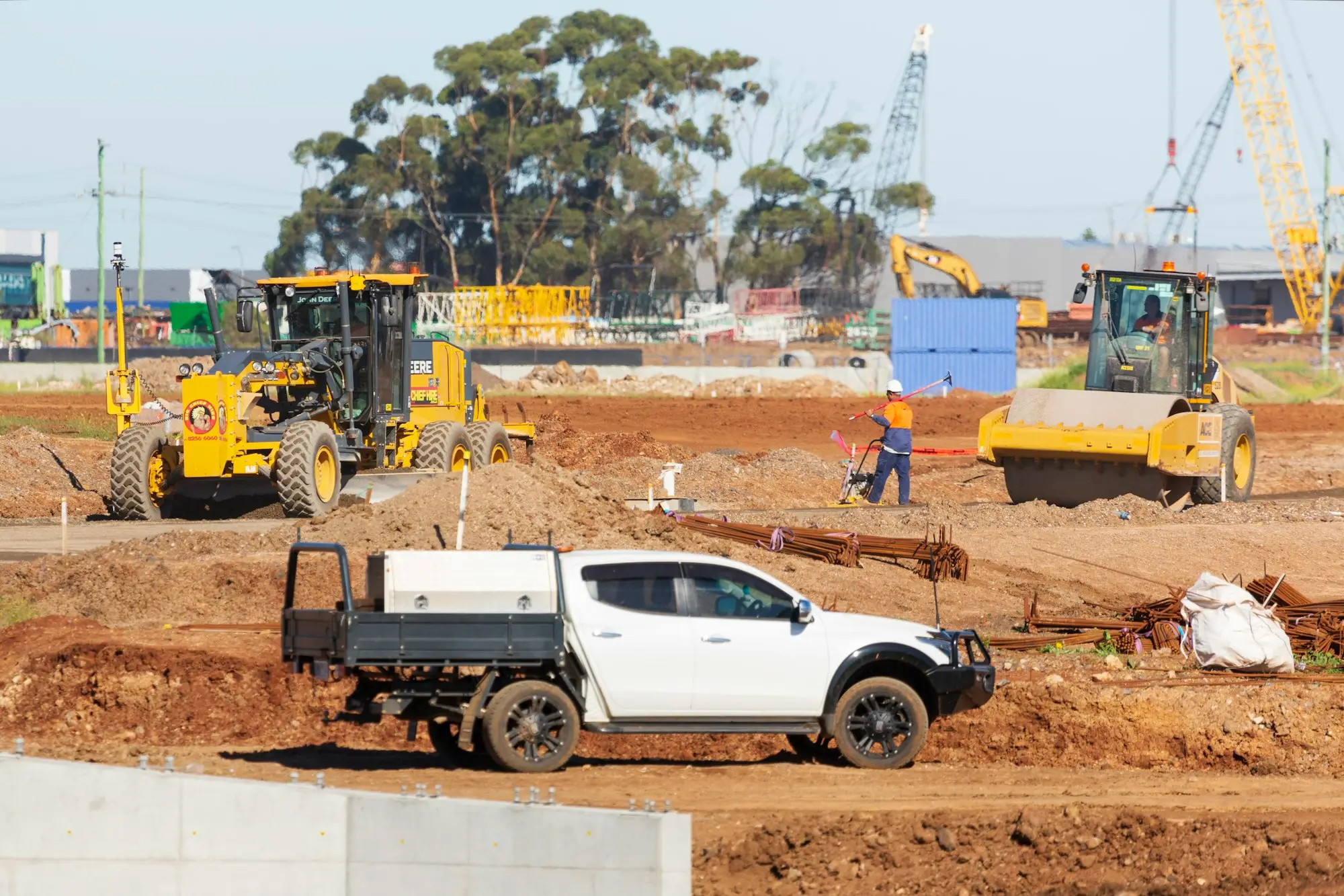 White tray-back ute parked on an Australian construction site with graders and rollers working behind it
