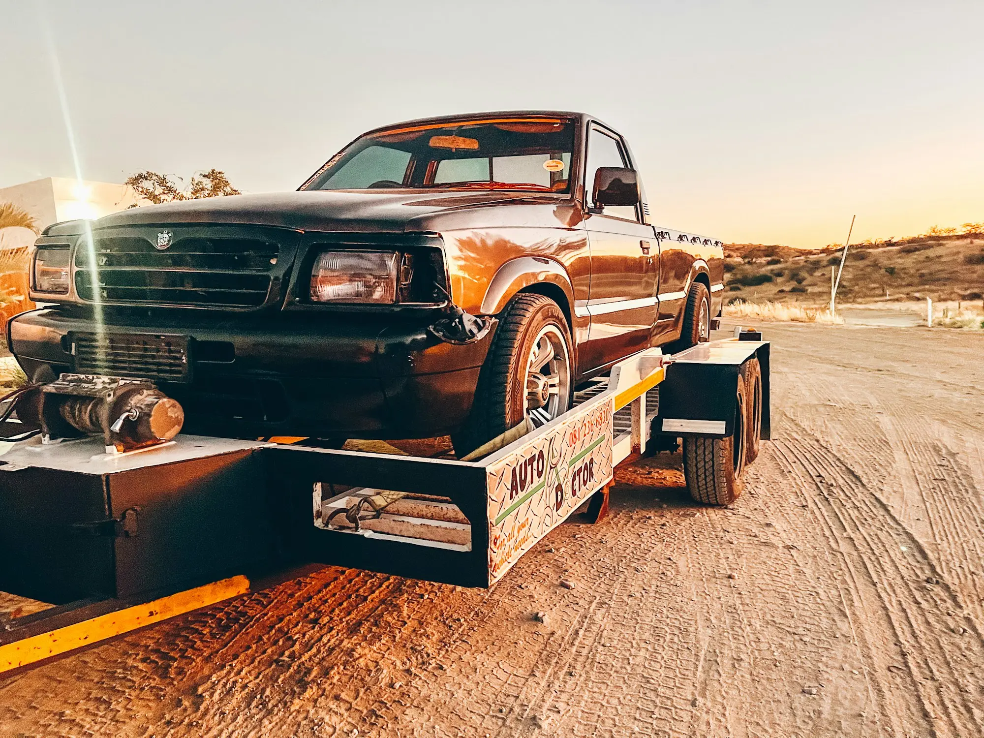 Ute loaded on a car trailer on a dusty Australian track at golden hour